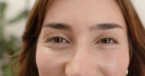 Smiling woman looking into camera closeup with natural skin texture and pearl earring