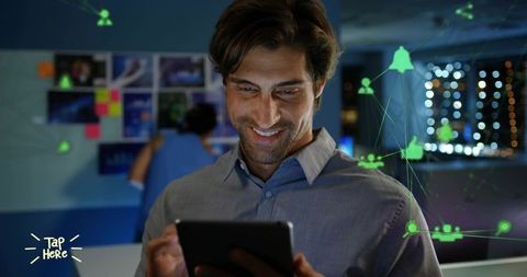 Smiling man holding tablet with glowing network overlay in collaborative office at night