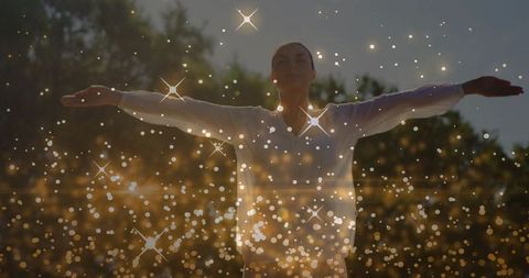 Woman Raising Arms Amidst Sparkling Lights in Natural Background