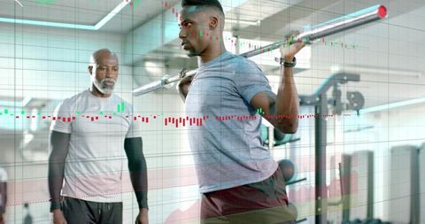 Young man squatting heavy barbell under coach supervision in gym with stock chart overlay