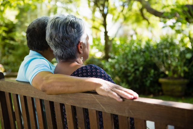 Senior couple sitting on a garden bench, enjoying a sunny day. Ideal for use in articles or advertisements related to retirement, senior living, outdoor activities, and peaceful lifestyles.