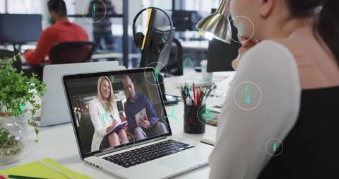 Remote team meeting showing woman watching laptop video call in modern open office