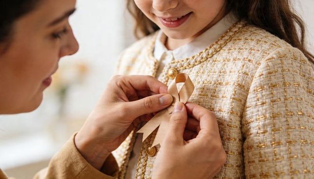 Parent pinning gold awareness ribbon on daughter wearing cream tweed jacket