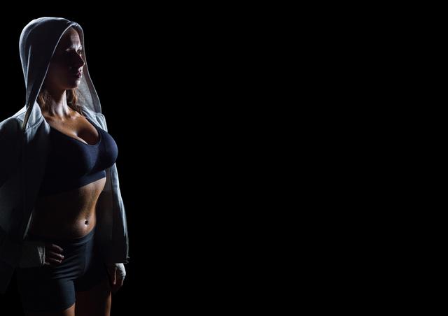 Female athlete in sportswear looking up confidently against a black background. Excellent for advertisements or articles related to fitness, health, and motivation. Can be used for gym promotions, women's empowerment campaigns, or workout gear branding.