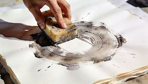 Hand pressing sponge creating circular ink wash on watercolor paper with deckled edges