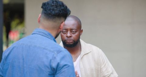 Two african american men talking seriously outdoors wearing denim and beige casual shirts