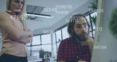 Team analyzing data on monitor with numerical overlay in modern collaborative office