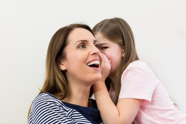 Mother and daughter sharing a secret moment at home. Perfect for illustrating family bonding, parenting tips, communication, and trust in family relationships. Ideal for use in family-oriented blogs, parenting articles, and advertisements promoting family values.