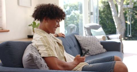 Happy Man Smiling at Smartphone on Cozy Blue Sofa