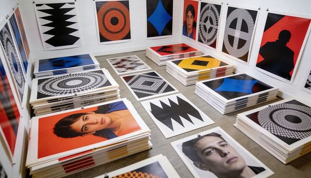 Stacking unframed art prints on studio floor with portraits and bold geometric patterns