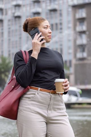 African american professional talking on phone by urban canal holding coffee and tote