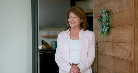 Senior Woman Greeting at Home Doorway with Festive Wreath in Kitchen