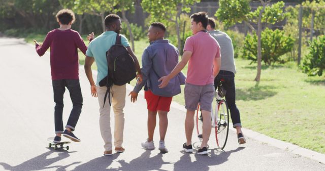 Happy diverse male friends walking with bicycle and talking on sunny day. spending quality time outdoors together.