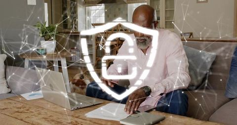 Senior man reviewing documents on laptop with digital security shield overlay for privacy