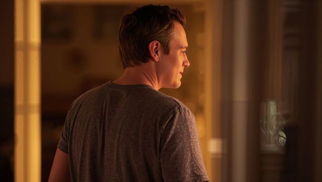 Contemplative man standing in warm home hallway with soft window reflections