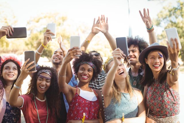Group of diverse friends taking selfies with mobile phones at an outdoor music festival. They are smiling and enjoying the moment, capturing memories together. Perfect for use in social media campaigns, advertisements for festivals, youth culture promotions, and technology-related content.