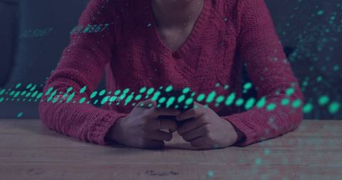 Woman holding smartphone at table with teal data overlay wearing pink sweater and necklace