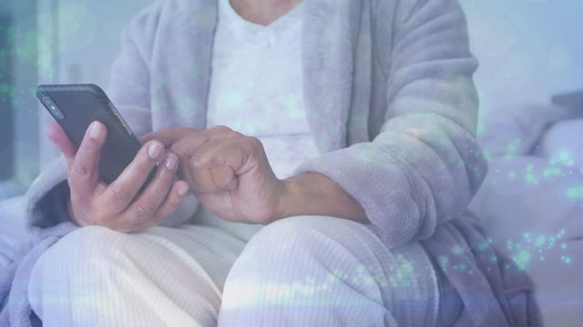 This portrays a senior African American woman relaxing at home while using a smartphone, suggesting a connection between technology and the elderly. Could be used in promoting technology accessibility, communication apps, elderly lifestyle, or healthcare services aimed at seniors.