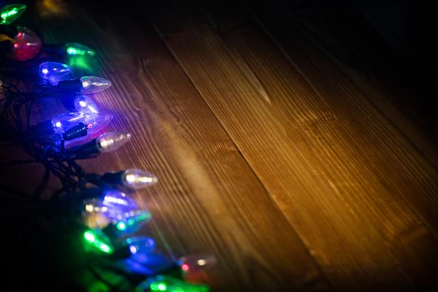 Colorful Christmas lights glowing on a wooden surface, creating a festive and warm atmosphere. Ideal for holiday-themed designs, festive greeting cards, seasonal advertisements, and social media posts celebrating Christmas and other winter holidays.