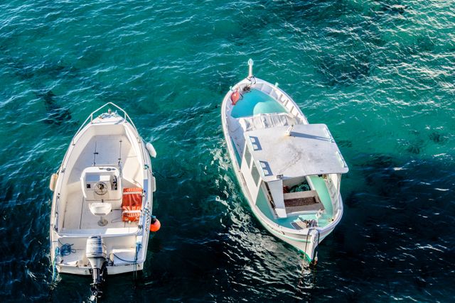 Two small fishing boats are moored side by side in clear turquoise water, creating a serene maritime scene. This visual can be utilized in travel promotions, marine life articles, aquatic adventure campaigns, or as a relaxing screensaver or background. The peaceful setting emphasizes calmness and natural beauty, suitable for outdoor and coastal themes.