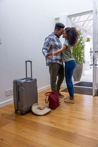 Couple holding hands and leaning foreheads in sunlit foyer with luggage