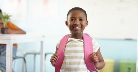 Smiling african schoolgirl wearing pink backpack standing in bright classroom