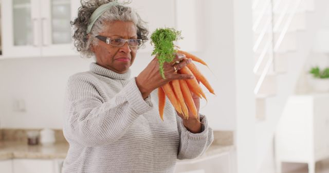 Happy senior african american woman cooking in kitchen, holding carrots. Retirement and spending time at home concept.