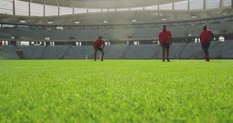 Rugby players standing on grass pitch in stadium wearing red jerseys preparing for match