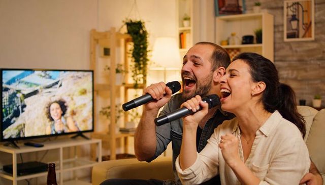 Couple singing karaoke on couch at home holding microphones and watching tv