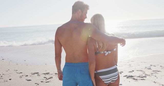 Couple embracing and enjoying sunset on beach. Possible use cases include travel brochures, romantic getaway promotions, lifestyle blogs, or advertisements for beachwear and sun protection products.