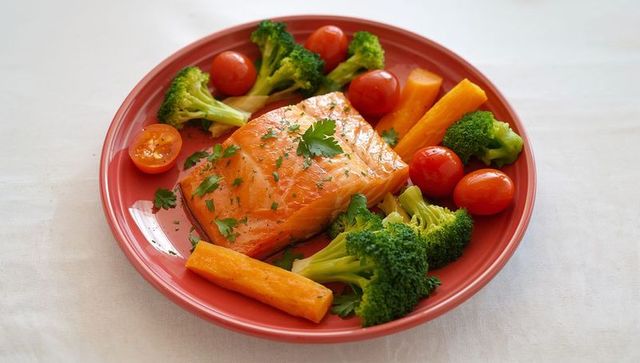 Glazed salmon fillet with steamed broccoli, cherry tomatoes and carrots on red plate