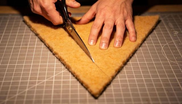 Craftsperson cutting triangular felt with shears on gridded cutting mat