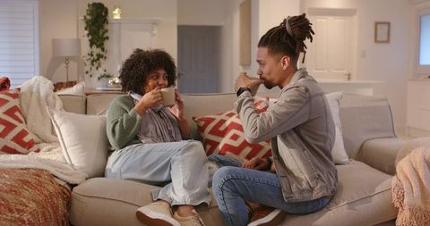 African american couple sharing cozy evening on sofa sipping hot drinks and conversing