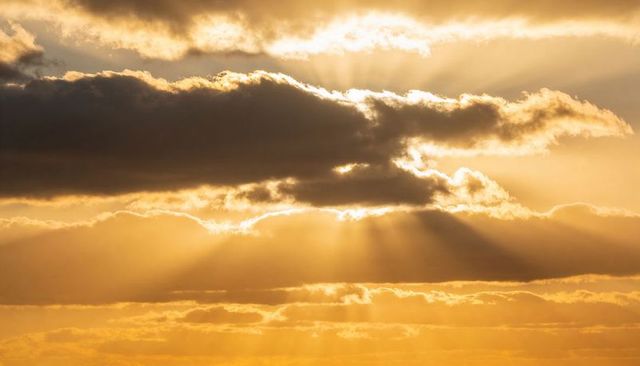 Sunbeams piercing layered clouds during golden sunset, dramatic crepuscular rays over horizon