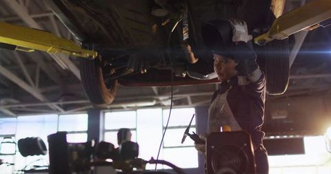 Female Welder Working Under Lifted Car on Two-Post Lift in Auto Repair Garage