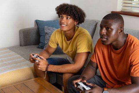 Diverse friends playing console game on couch in cozy modern living room