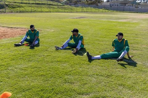 Baseball team stretching on outfield grass in green yellow uniforms during practice