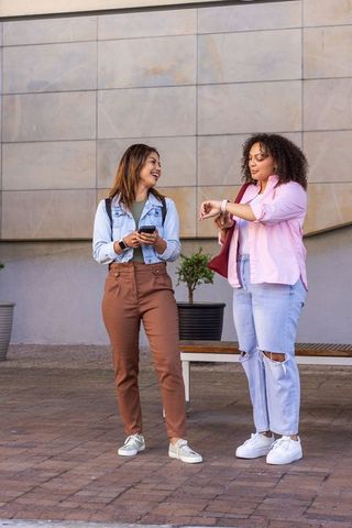 African american friends chatting and checking time with phone and watch on urban plaza