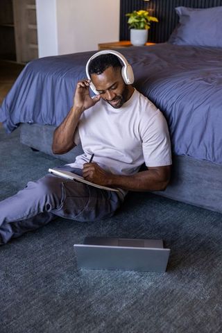 Mature african american man listening with headphones and journaling on bedroom floor