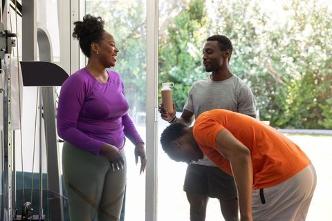 African american friends training together in sunlit home gym by glass doors