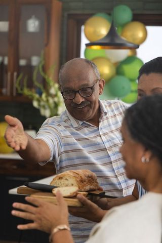 Senior african american man serving sliced bread to family in cozy kitchen gathering