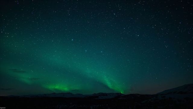 Emerald aurora borealis glowing over snowy tundra and mountain silhouettes under starry sky