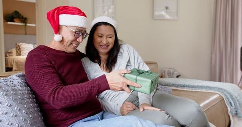 Couple with santa hats sharing holiday gift on cozy couch