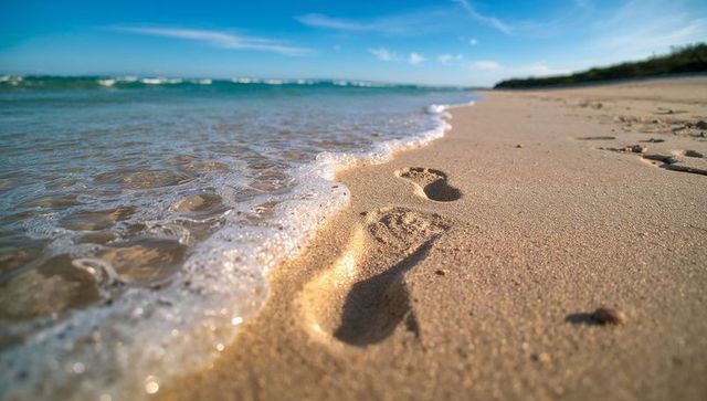 Barefoot footprints in wet sand with foamy waves on tropical beach morning