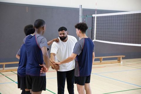 Indian coach leading diverse teenage volleyball team huddle in indoor gymnasium