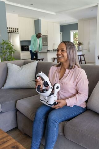 African american woman using neck massager on sofa while partner on laptop in living room