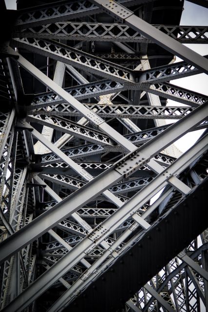 Close-up of the underside of a metal bridge showcasing its steel beams and cross girders. This can be used in projects focusing on architecture, forensic engineering studies, construction materials, or as a background in urban industrial themes.