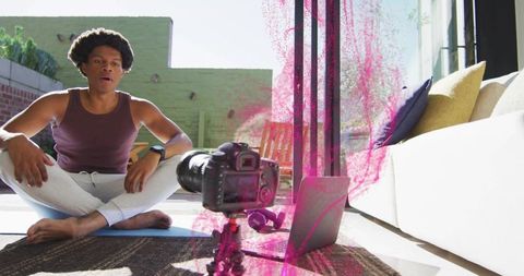 Man leading and filming home workout with dslr and laptop on living room mat