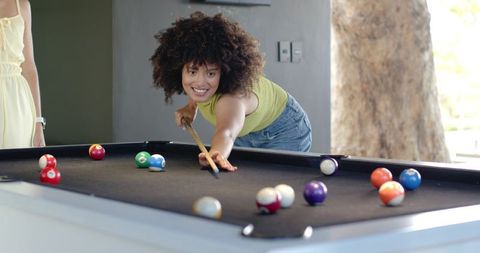 Diverse friends playing pool and smiling while aiming shot on black-felt table
