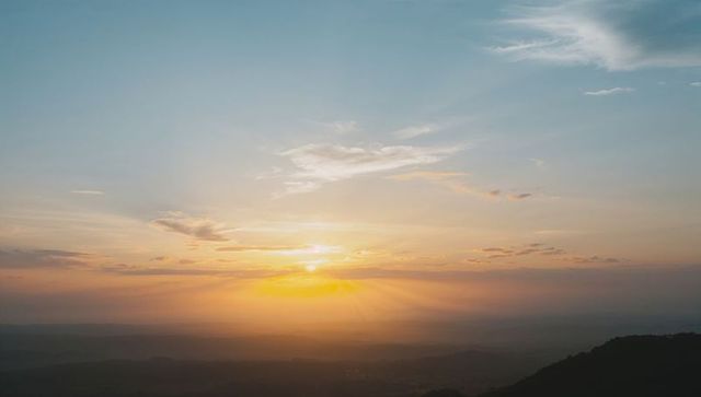 Golden sunrise casting radiant rays over layered mountain ridges and misty valley